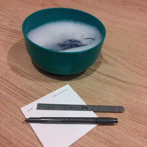 a plastic bowl with sudsy water and some knitting. a post it with "gauge" handwritten, a pen, and a small ruler is in front of the bowl