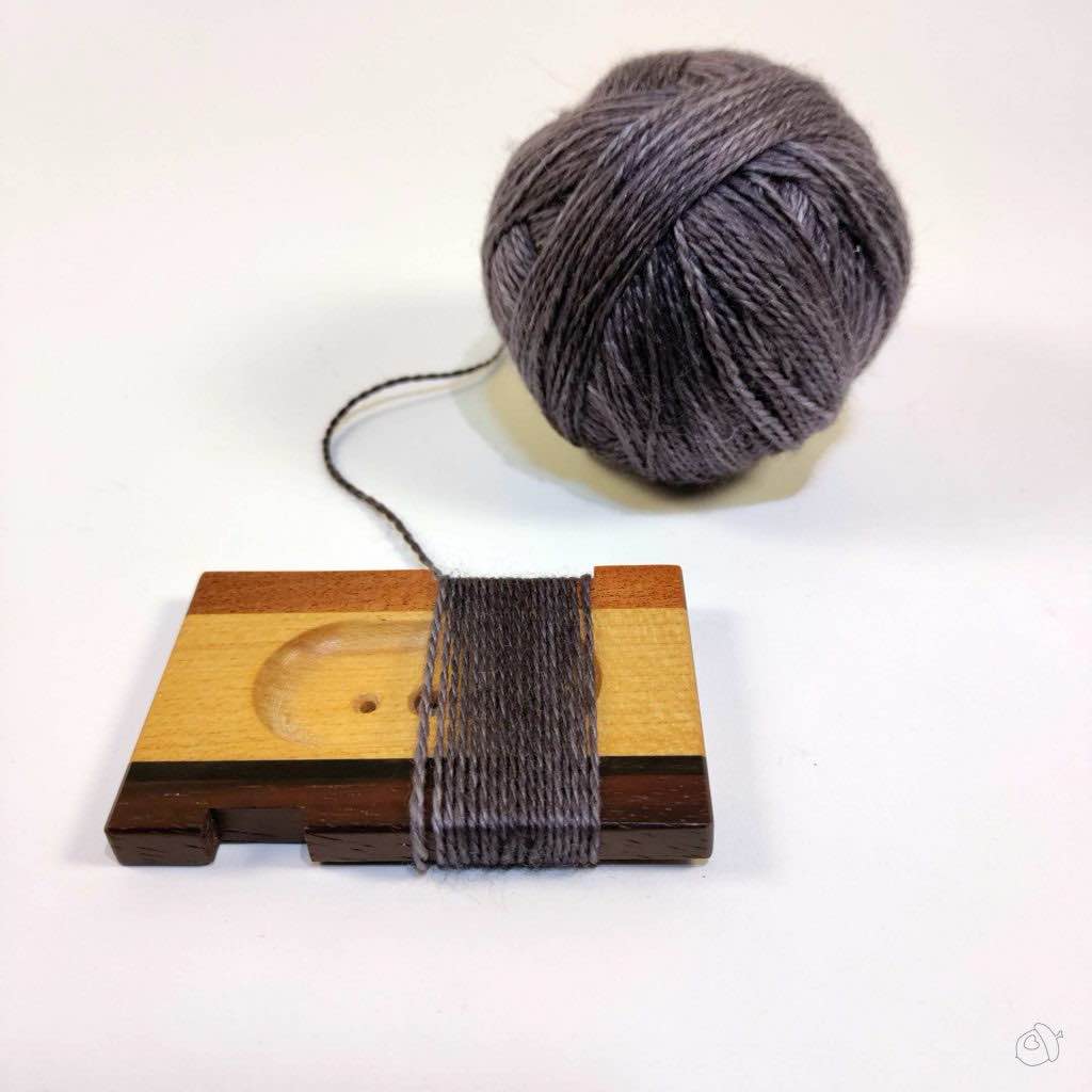 Handspun ball of Anzula Cloud and WPI tool with yarn wrapped around it on a plain white background