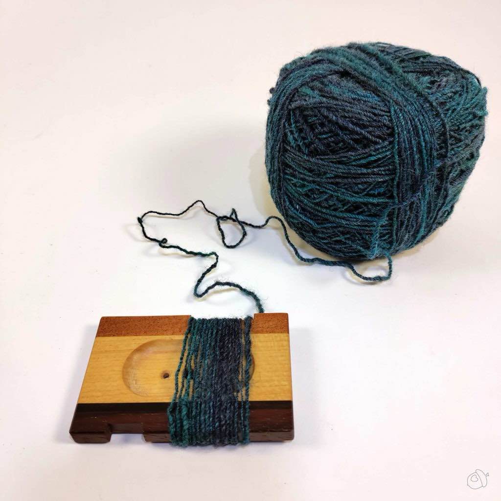 cake of handspun and WPI tool with yarn wrapped around it on a plain white background