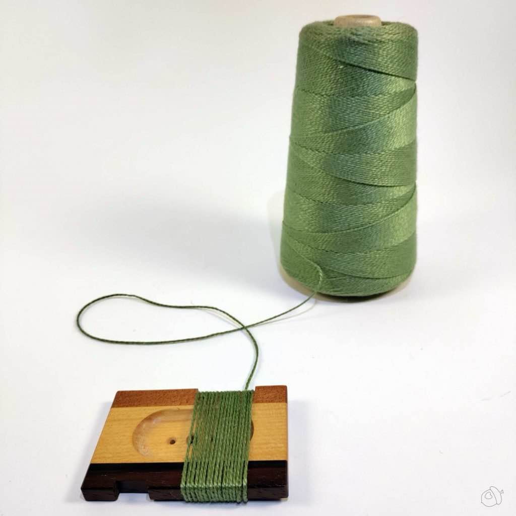 Cone of persian green UKI 3/2 cotton and WPI tool with yarn wrapped around it on a plain white background