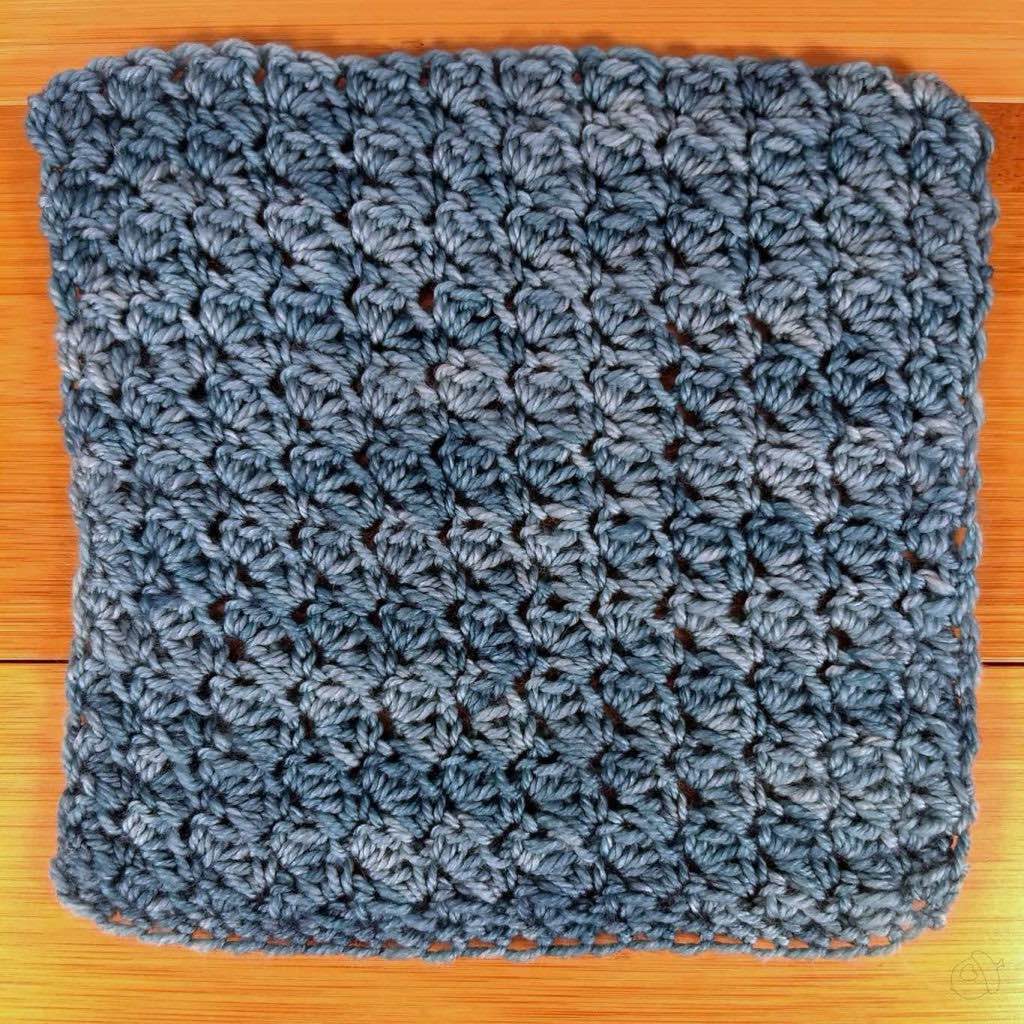 squishy fingering weight yarn in aqua color, crocheted in a simple textured crochet stitch. Shown flat on a wooden surface.