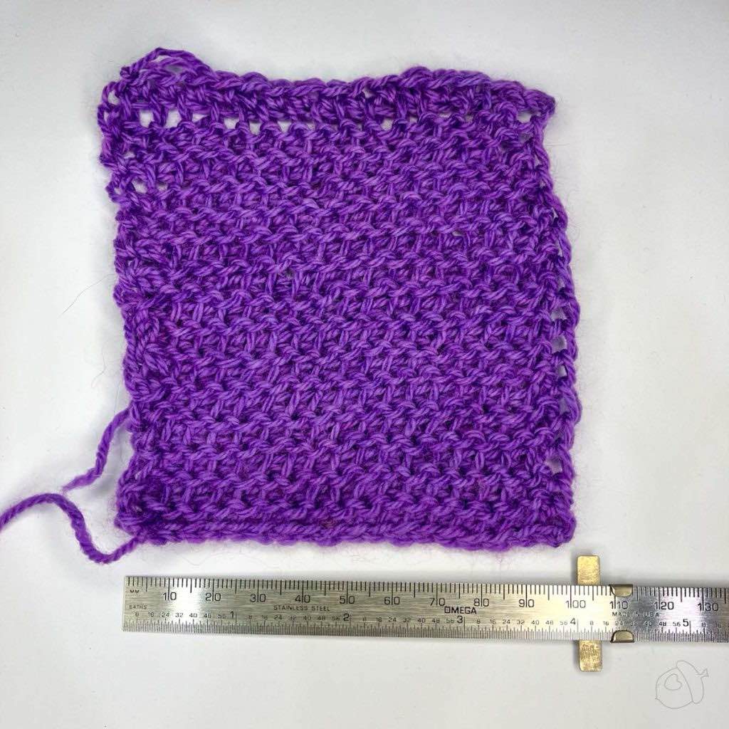 purple Tunisian Purl Stitch swatch in Artyarns Merino Cloud, unblocked it is on a white background next to a ruler showing approximately 4 in / 10 cm width.