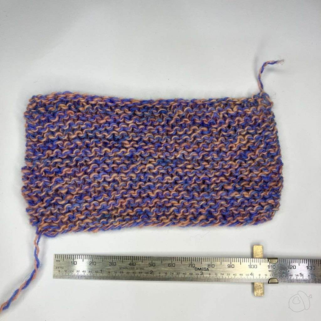 blue/pink marled yarn garterstitch swatch in Plied North Ave, un blocked it is on a white background next to a ruler showing approximately 4 in / 10 cm width.