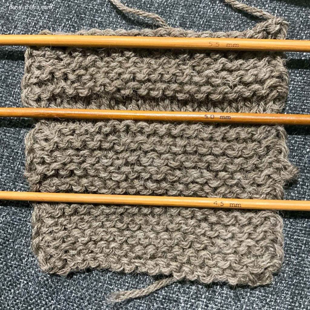 Fishermen's Wool In garter stitch with needles ona grey fabric background 