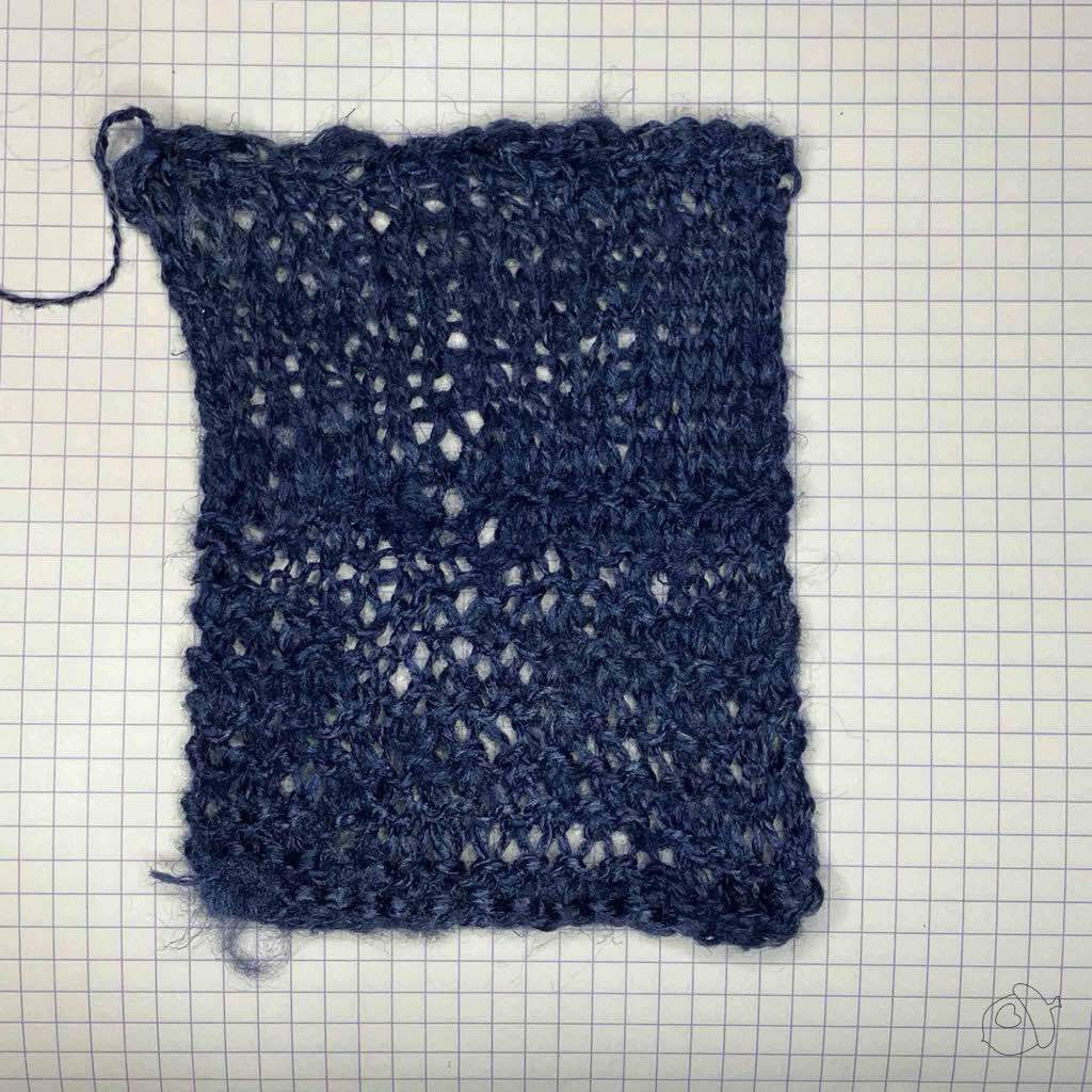 Knit stockinette and garter stitch swatch in ColourMart fingering weight crepe style silk bakketta, dark blue. blocked and laid flat on grid paper